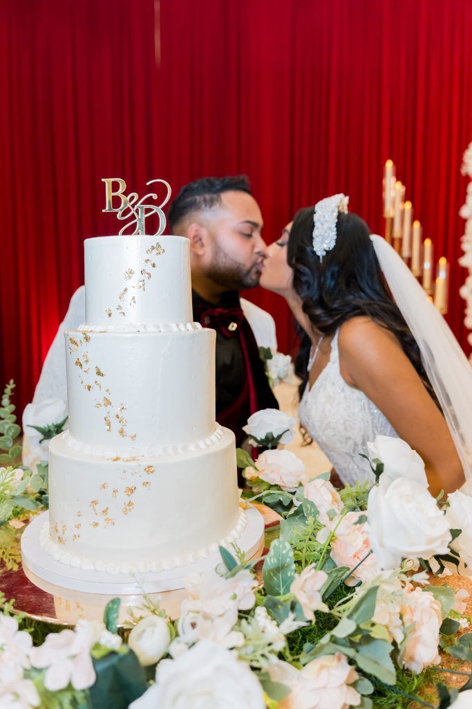 bride and groom kissing behind a white and gold, 3-tier wedding cake by bells cake house