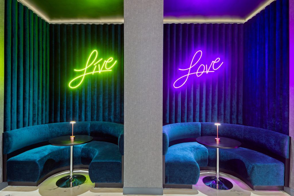 Nook seating with dark, midnight blue lounge couches and drapes with neon Live and Love signs