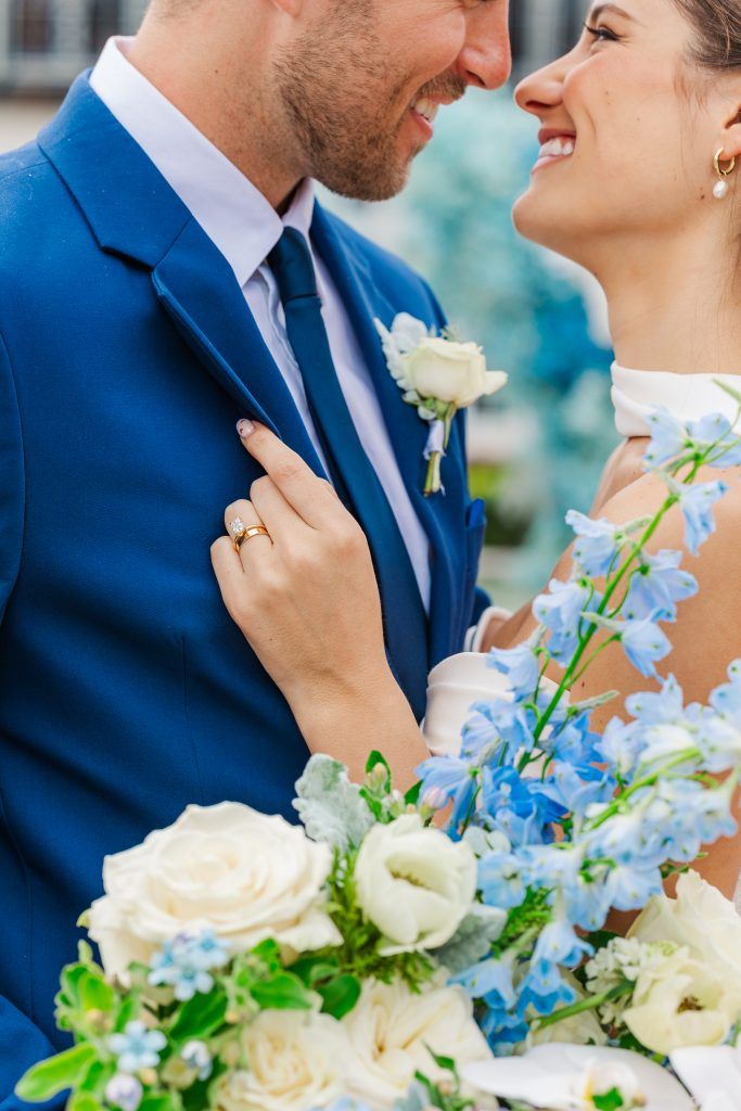 Bride and groom smiling at each other with white and blue bridal bouquet in front