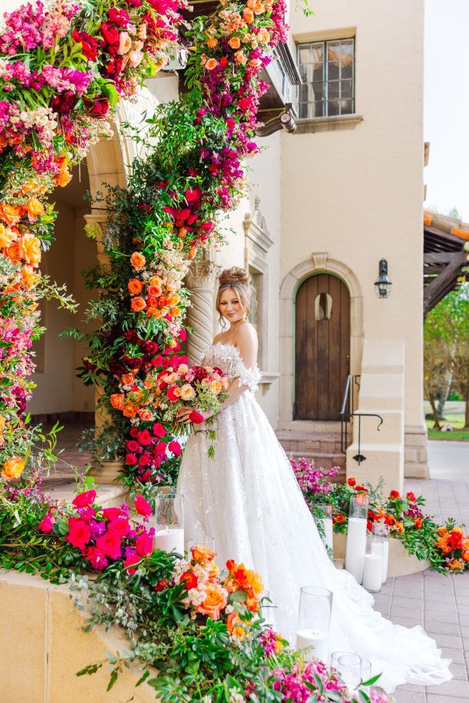 Bride holding large brightly colored bouquet with bright floral and green archway