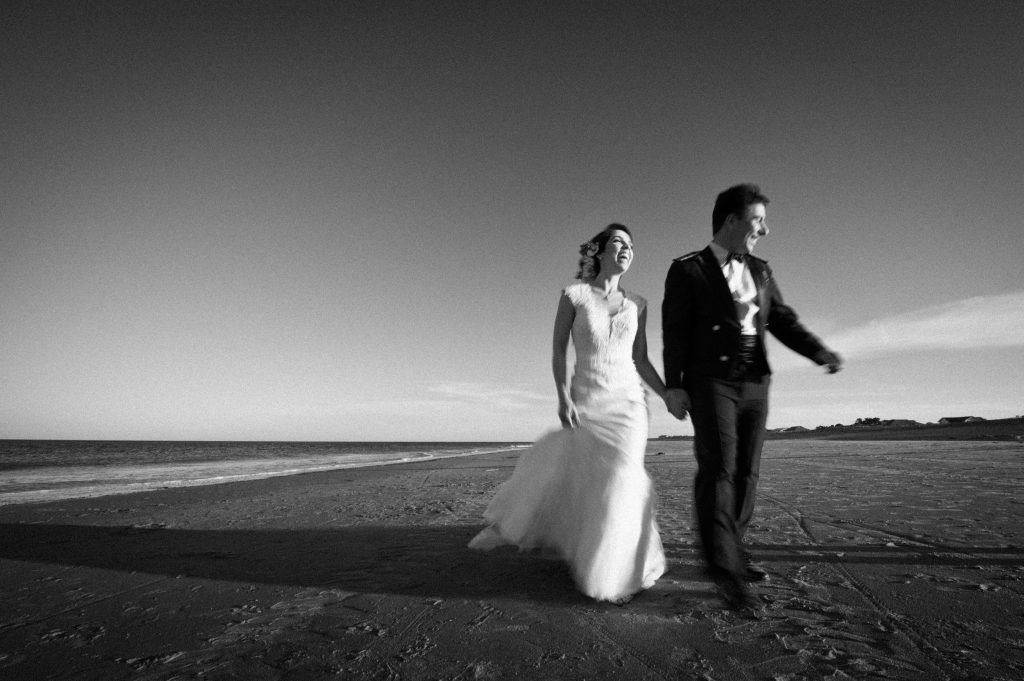 black and white photo of bride and groom walking on the beach