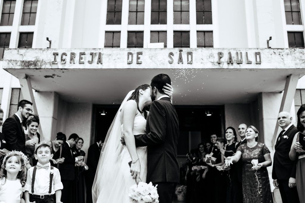 black and white photography of bride and groom kissing with loved ones around