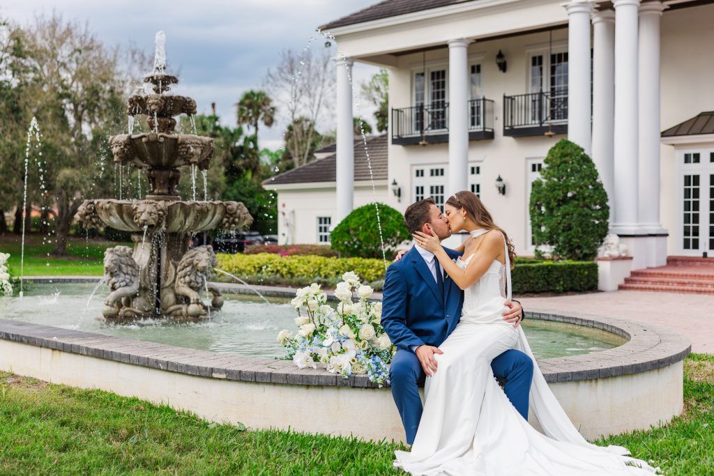 bride and groom kissing with blue and white florals behind them on a water fountain