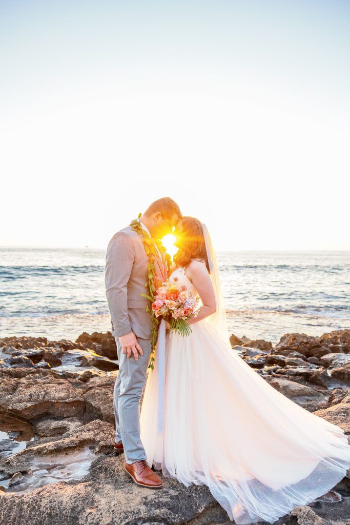 bride and groom touching foreheads together on rocky beach at sunset