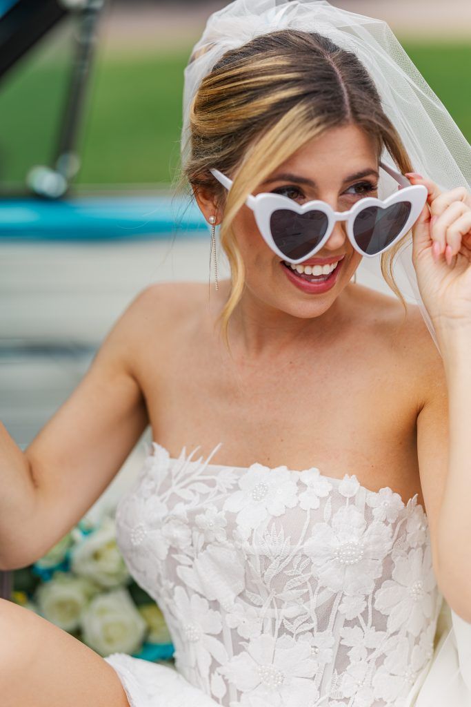 bride smiling into the distance wearing a floral lace dress and heart glasses