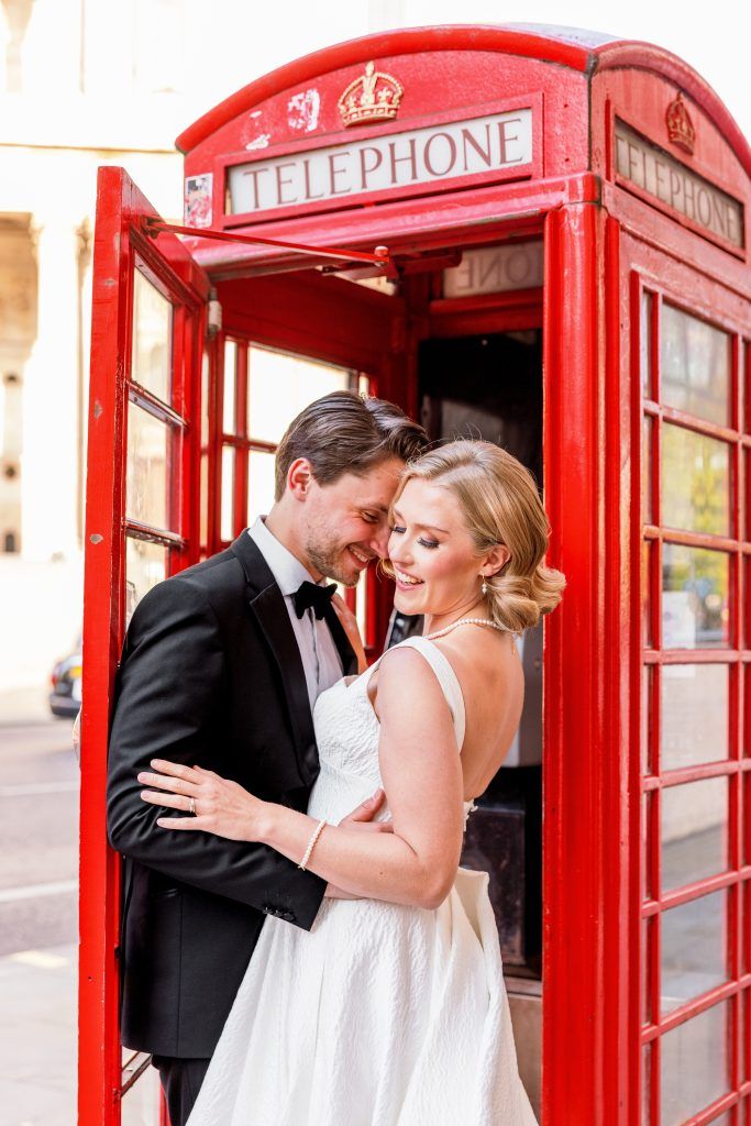 groom holding brides waist as she looks over her shoulder at a red telephone booth