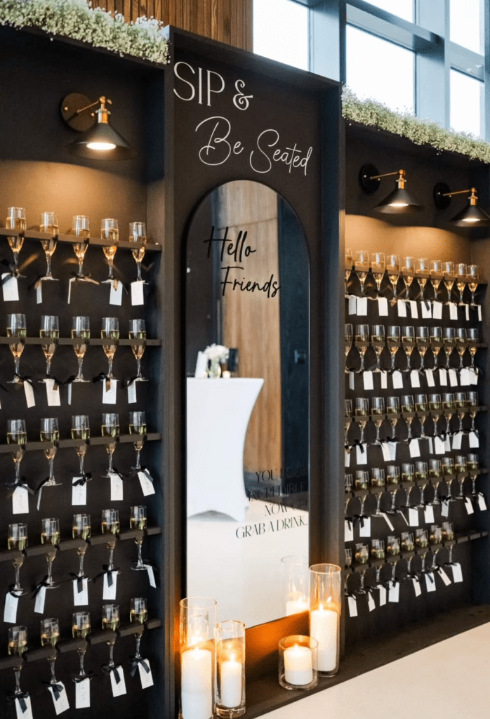 Black champagne wall with candles at the base and a mirror centered among the wall of champagne glasses