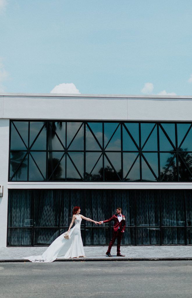 Bride and groom pose in front of a modern building exterior at DoubleTree by Hilton Orlando, holding hands across the sidewalk.