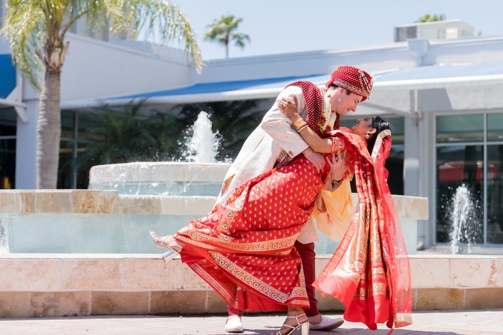 Groom dips bride in vibrant traditional Indian wedding attire near the fountain at DoubleTree by Hilton Orlando.
