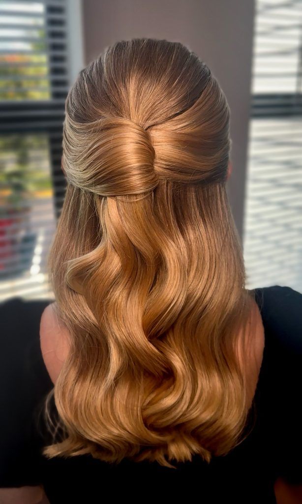 Blonde hair styled in polished waves with a sleek half-up twist for a timeless bridal look.