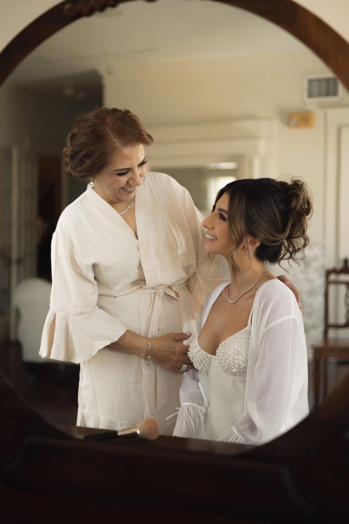Mother and bride share a joyful moment while getting ready, the bride with a natural soft glam makeup.