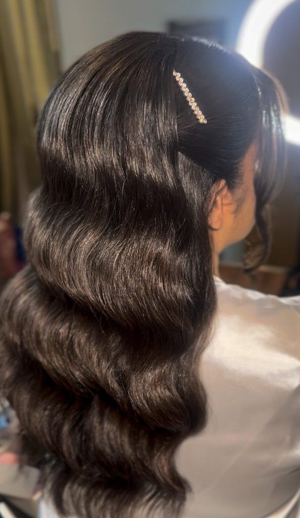 Dark brunette hair styled in deep glossy waves with a sparkling barrette clipped to the side.
