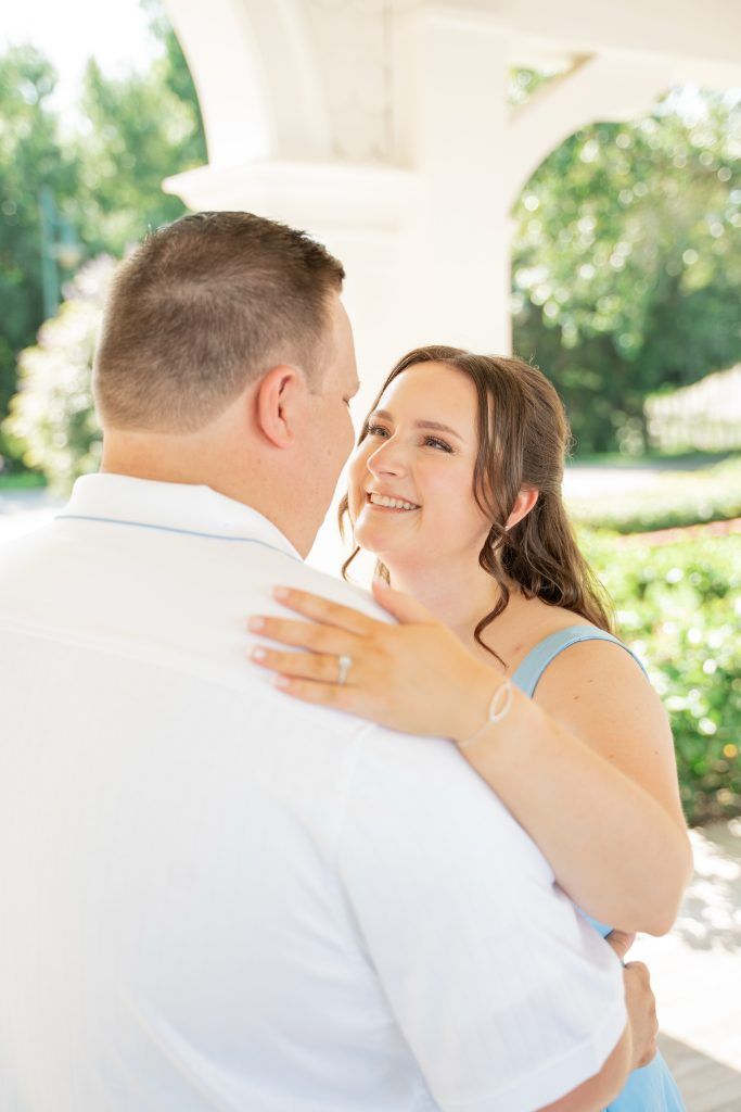 Woman in a light blue dress smiles lovingly at her partner in a white shirt during an outdoor engagement session.