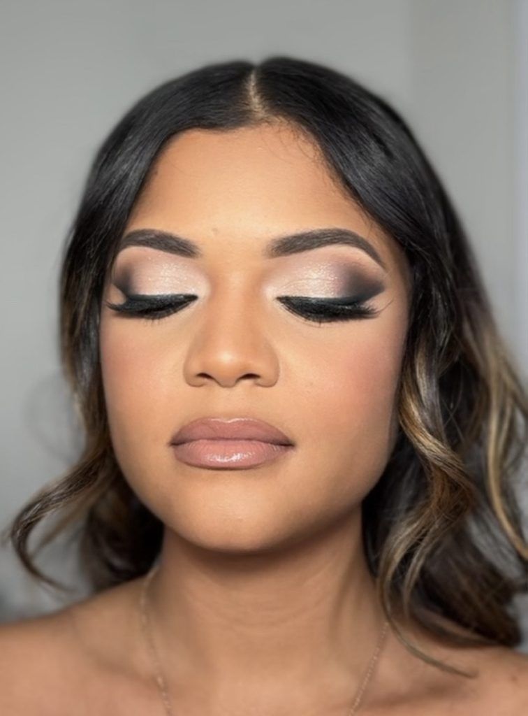 Woman with dramatic smokey eye makeup, nude lips, and curled hair looks serene with her eyes closed.