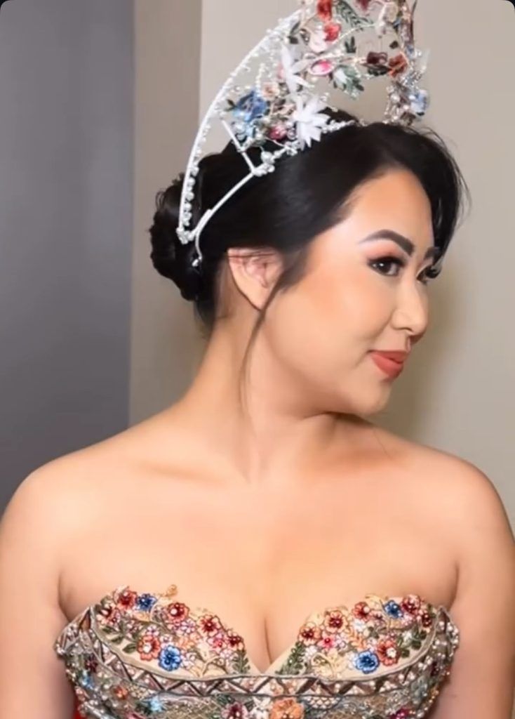 Bride in an embellished strapless gown with multicolor floral details wears an elaborate jeweled crown, looking to the side.