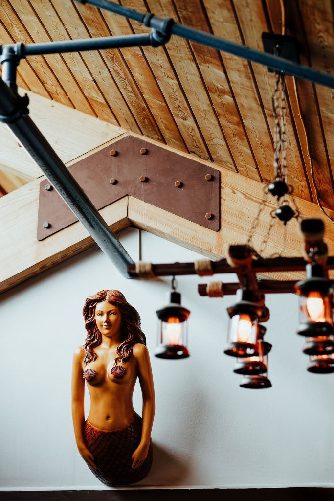 Wooden carved mermaid wall decor mounted under a peaked ceiling with rustic lantern-style lights hanging nearby.