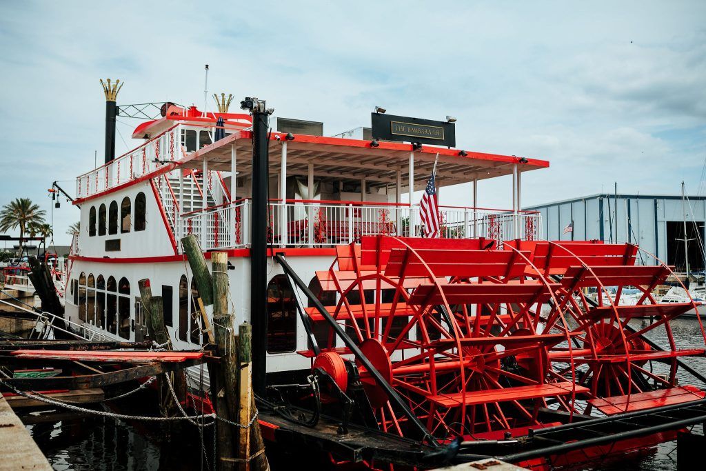 Exterior of a large red-and-white paddlewheel riverboat named "the Barbara-Lee," docked by the marina.