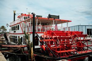 Exterior of a large red-and-white paddlewheel riverboat named "the Barbara-Lee," docked by the marina.