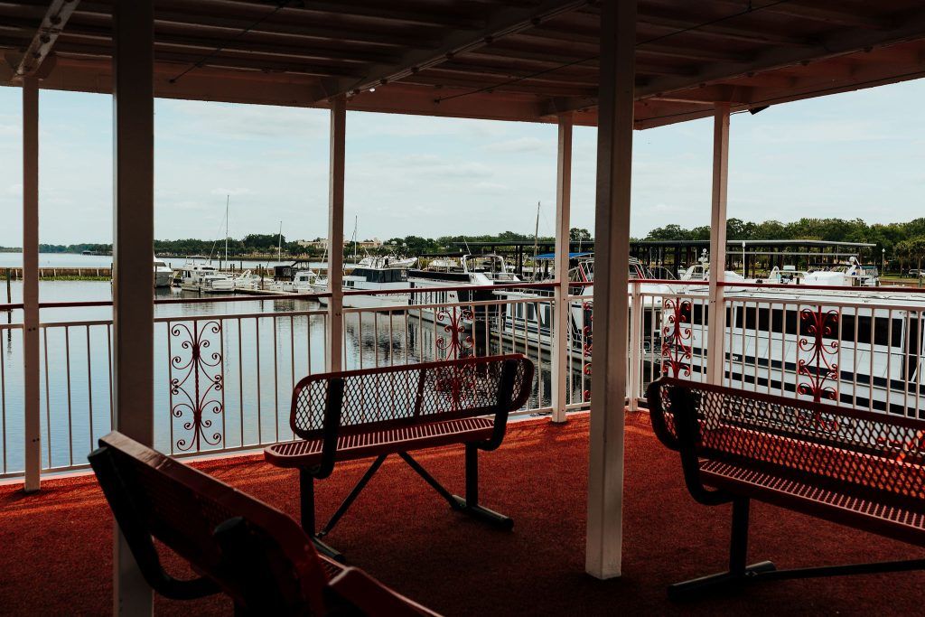 Outdoor deck seating with red benches overlooking a marina filled with docked boats.