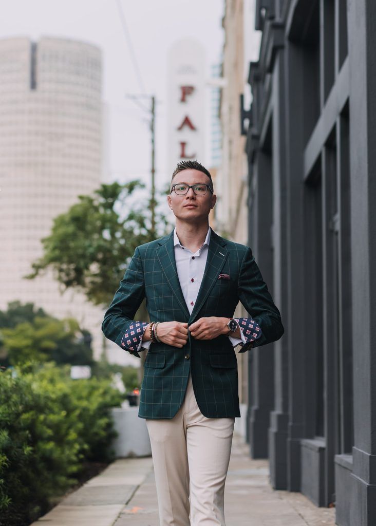 a man walks toward the camera fixing his green suit jacket, wearing tan dress pants and a blue undershirt