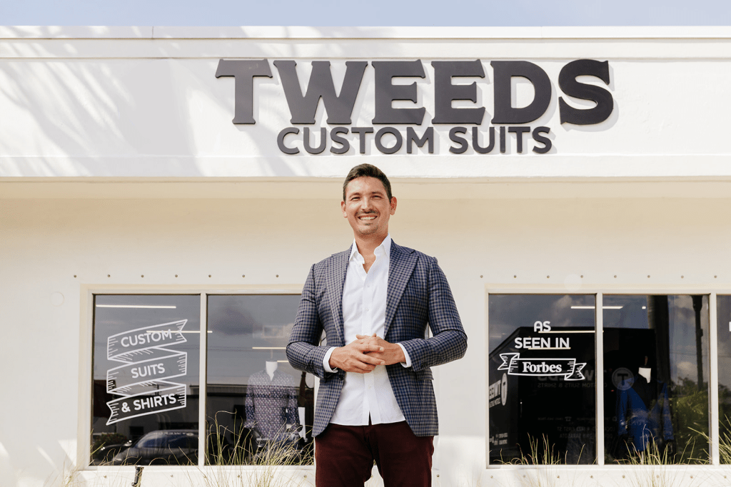 man wearing dark maroon pants and a grey patterned suit jacket standing in front of TWEEDS Custom Suits shop