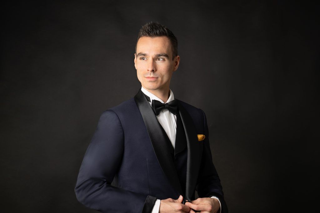 Man in black suit with gold pocket square looking off in the distance over his right shoulder