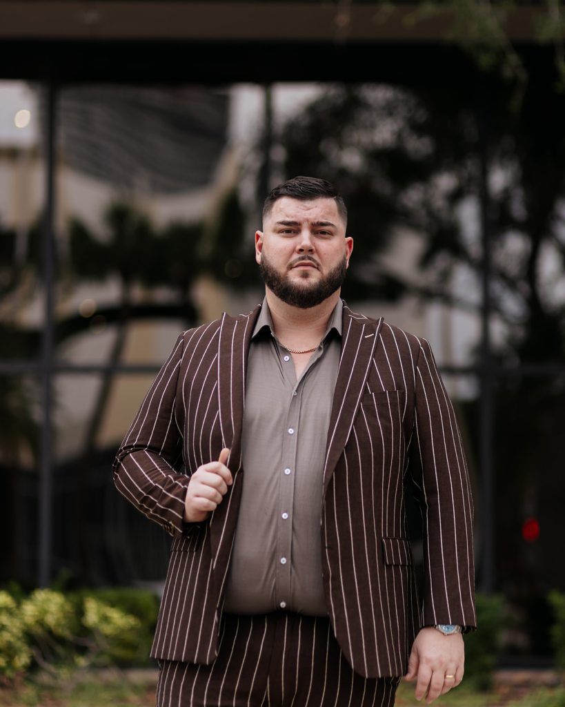 man wearing a light brown undershirt and a dark brown suit with white stripes