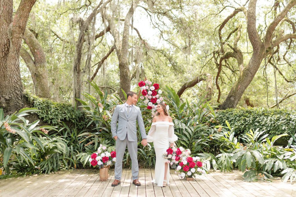 a couple standing in an outdoor garden, surrounded by red, pink, and white florals