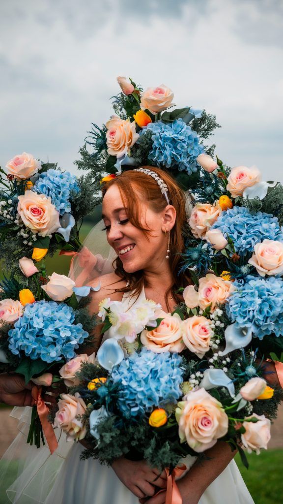 a joyful bride surrounded by lush blue hydrangeas and soft peach roses